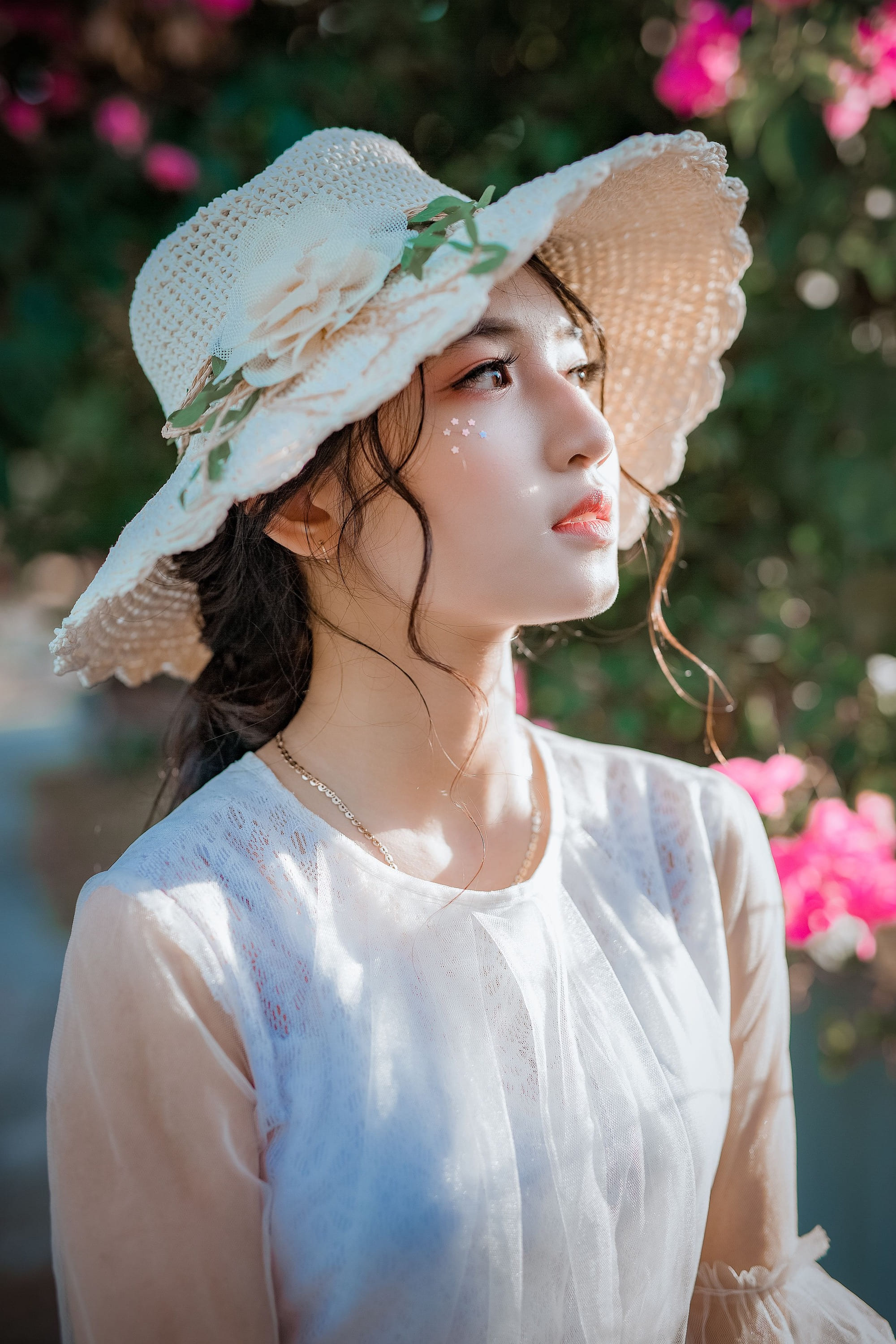 A woman in a straw hat among roses, looking away